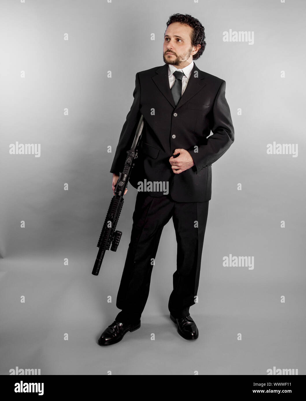 Unternehmer im schwarzen Anzug und mit Maschinengewehr auf grauem Hintergrund bewaffnete Stockfoto