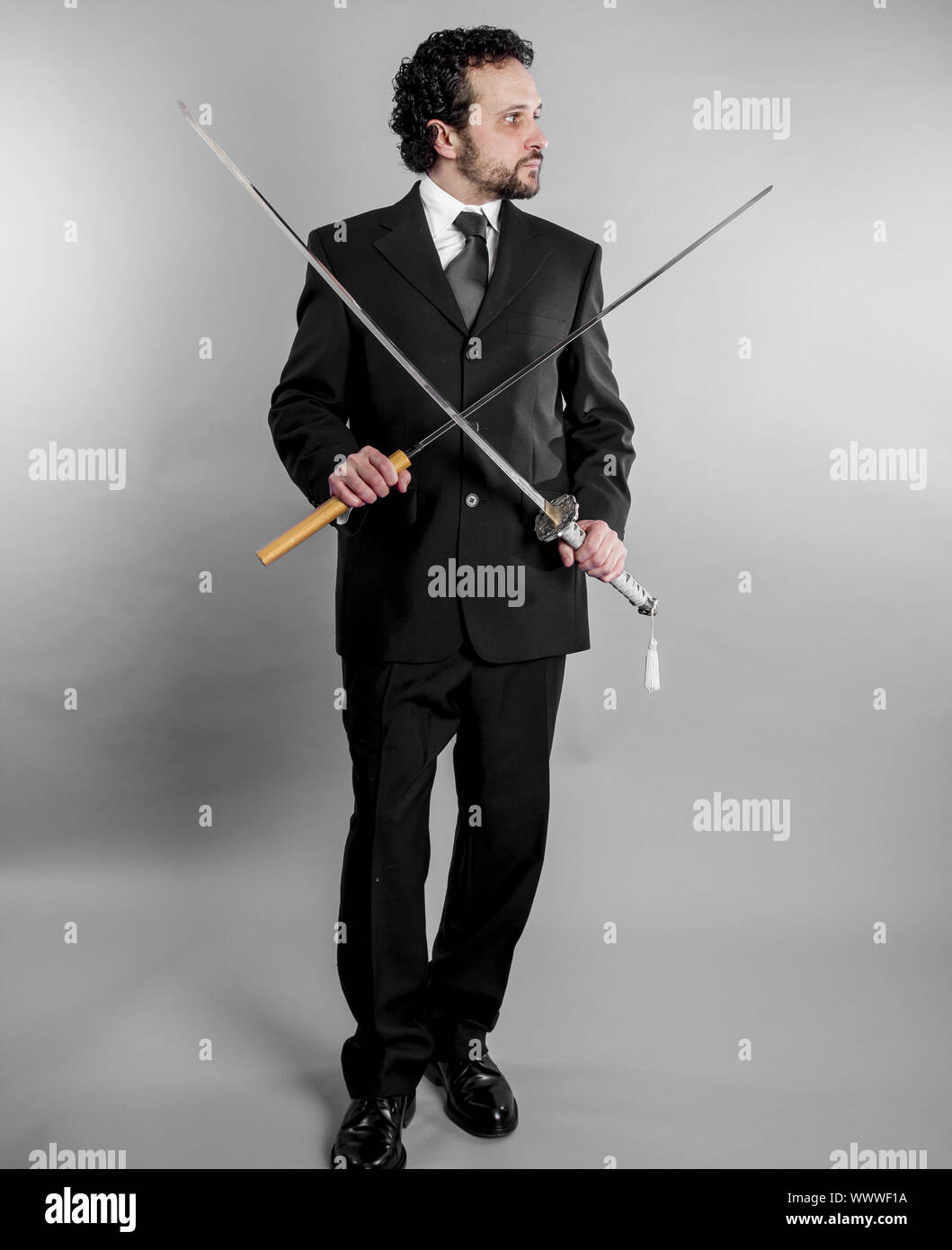 Unternehmer im schwarzen Anzug und bewaffneten japanisches Schwert auf grauem Hintergrund Stockfoto