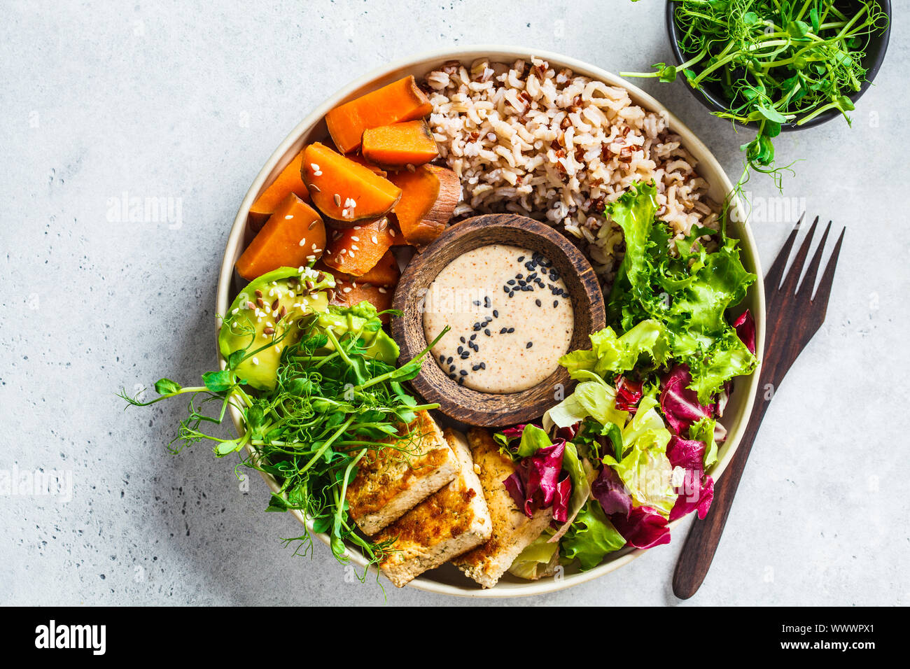 Buddha Schüssel mit Tofu, Avocado, Reis, Sämlinge, Süßkartoffel und tahini Dressing. Veganes essen Konzept. Stockfoto