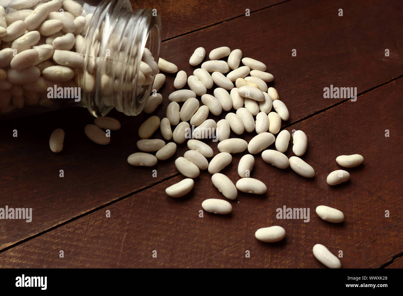 Trockene weiße Bohnen verschütten aus einem jar auf einem rustikalen Holztisch Stockfoto