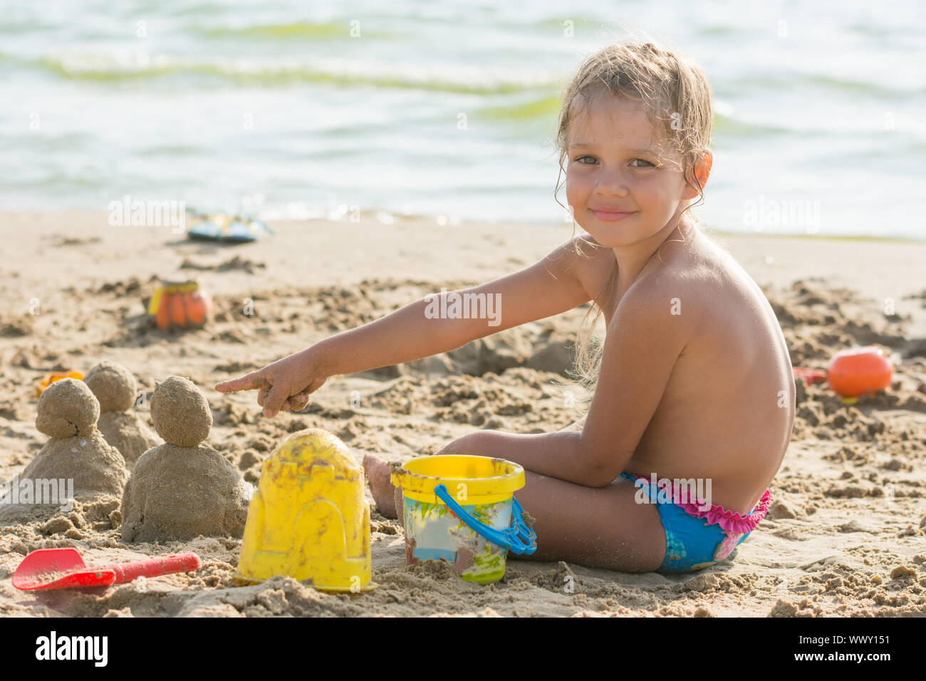 Zufrieden mit dem Kind auf einem sandigen Strand an den Wasser-Points im Kuchen von Sand eingestellt Stockfoto