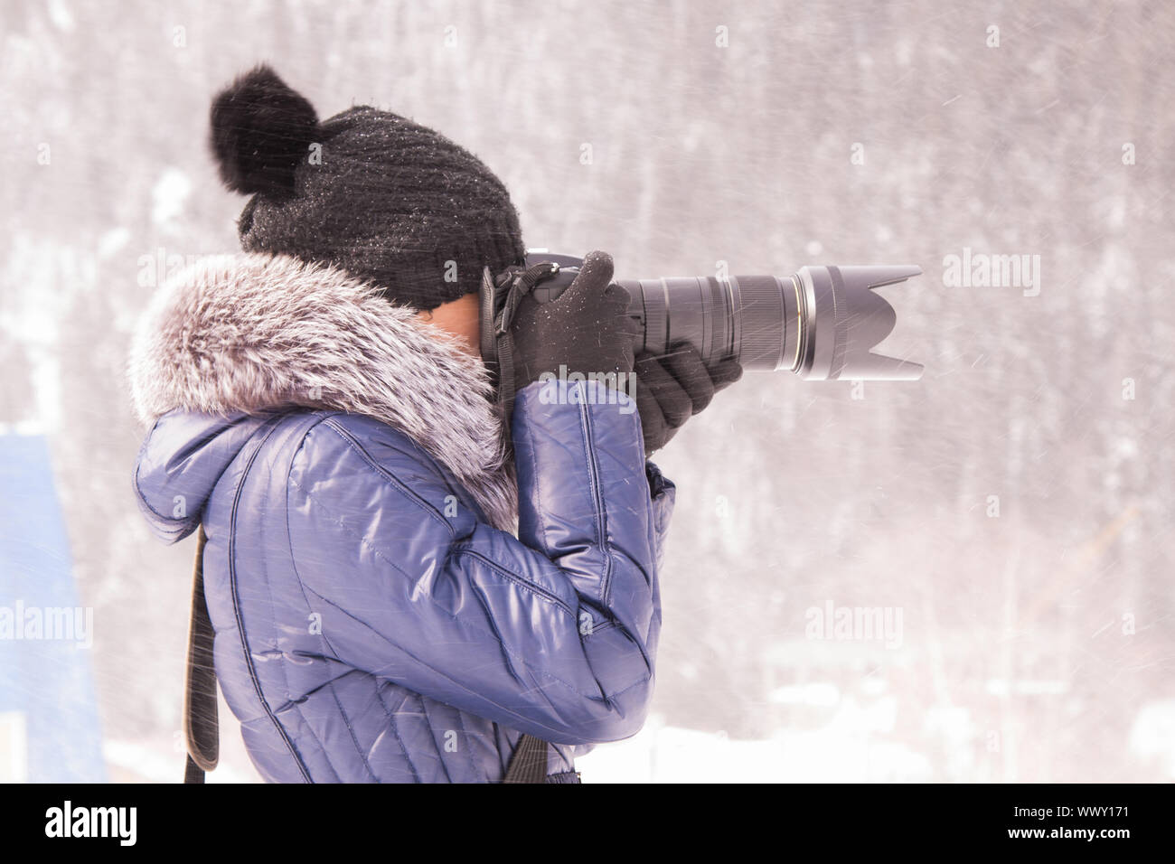 Junges Mädchen im Winter in einem Schneesturm auf eine SLR-Kamera mit Teleobjektiv fotografiert Stockfoto