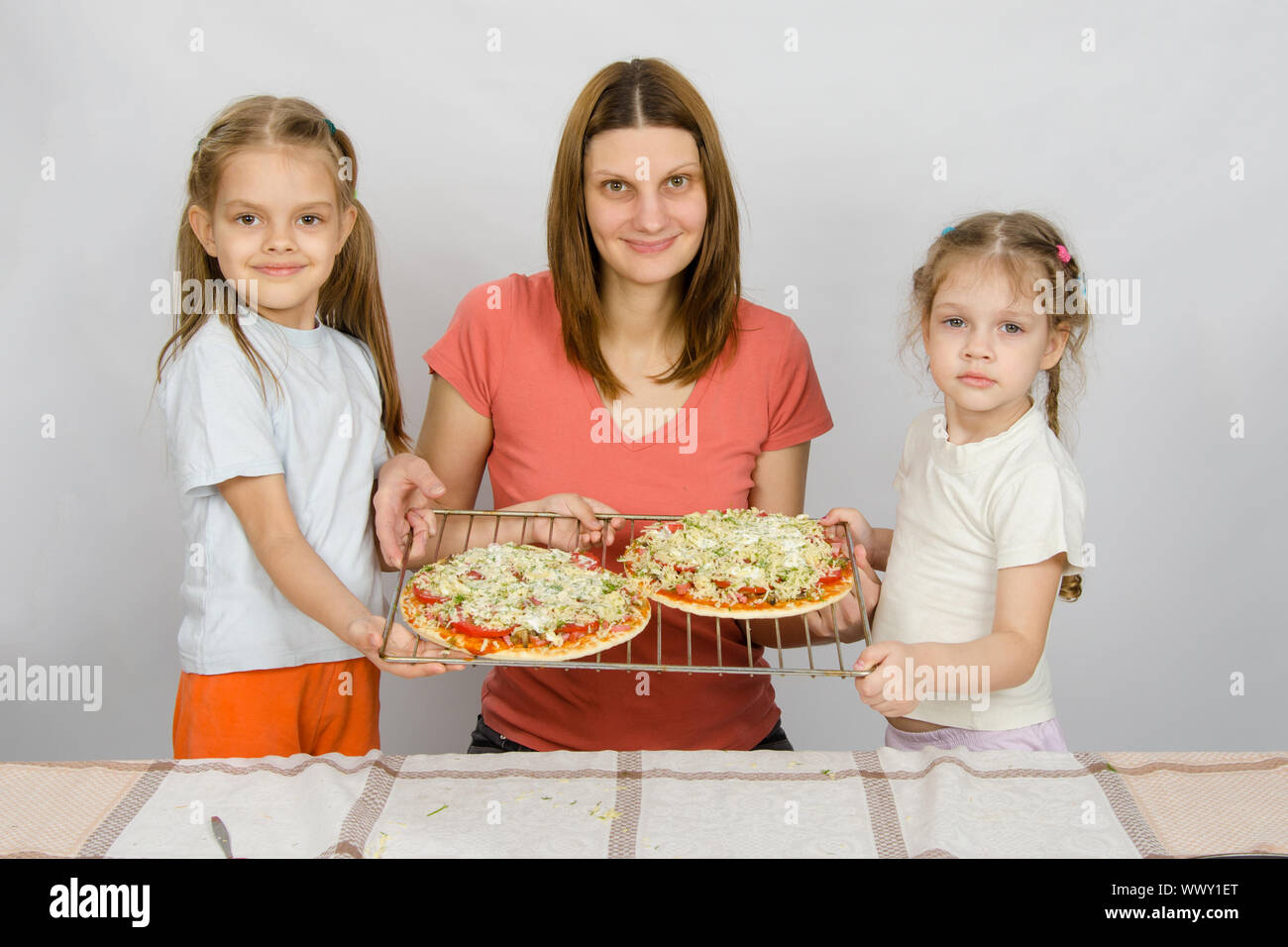 Mutter und zwei kleinen Töchtern zeigen, dass die beiden noch nicht gebackenen Pizza auf einem Backblech gemacht hatte Stockfoto