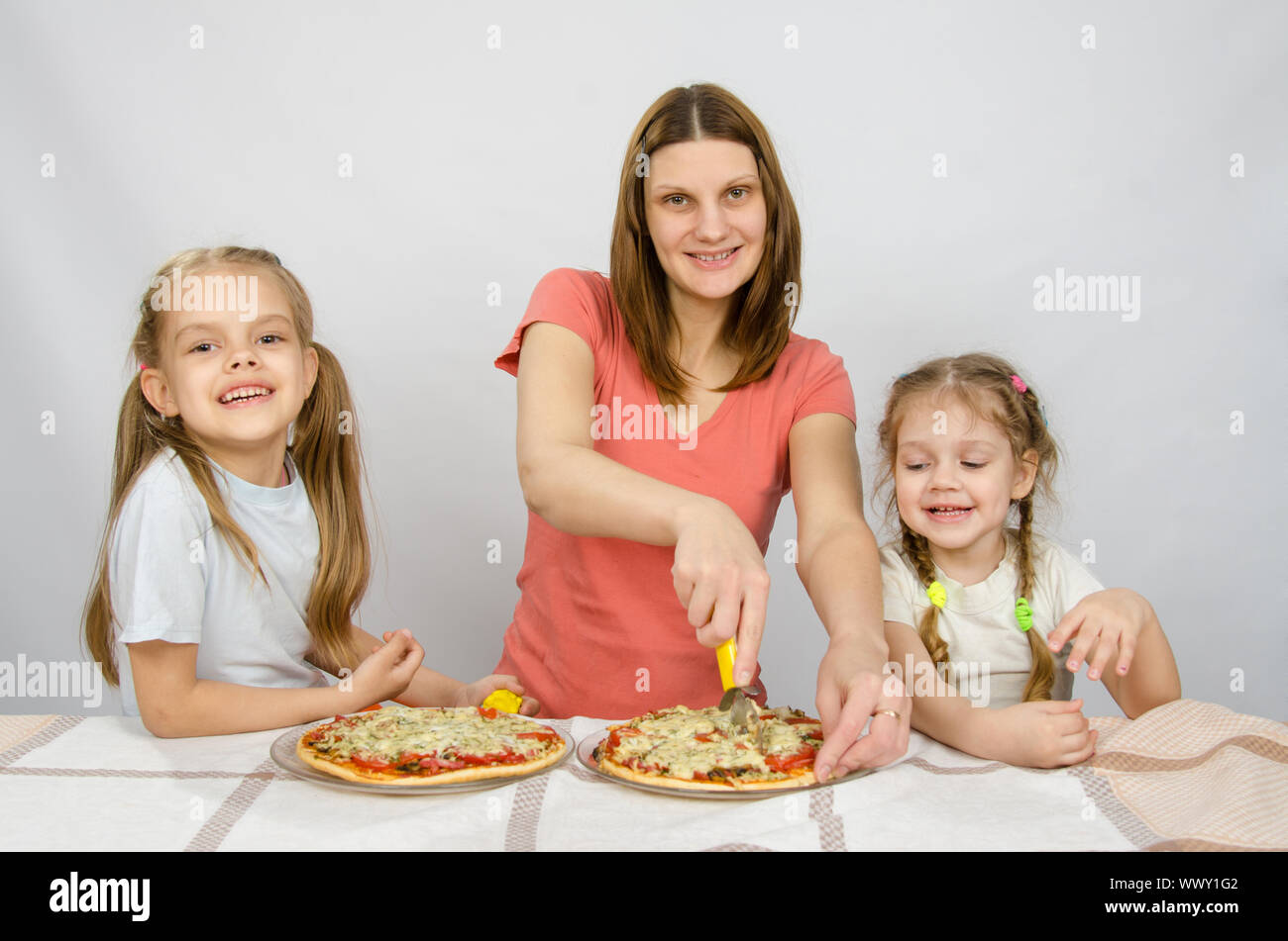 Mutter und zwei kleinen Töchter glücklich sitzt an einem Tisch mit zwei Pizzen Stockfoto