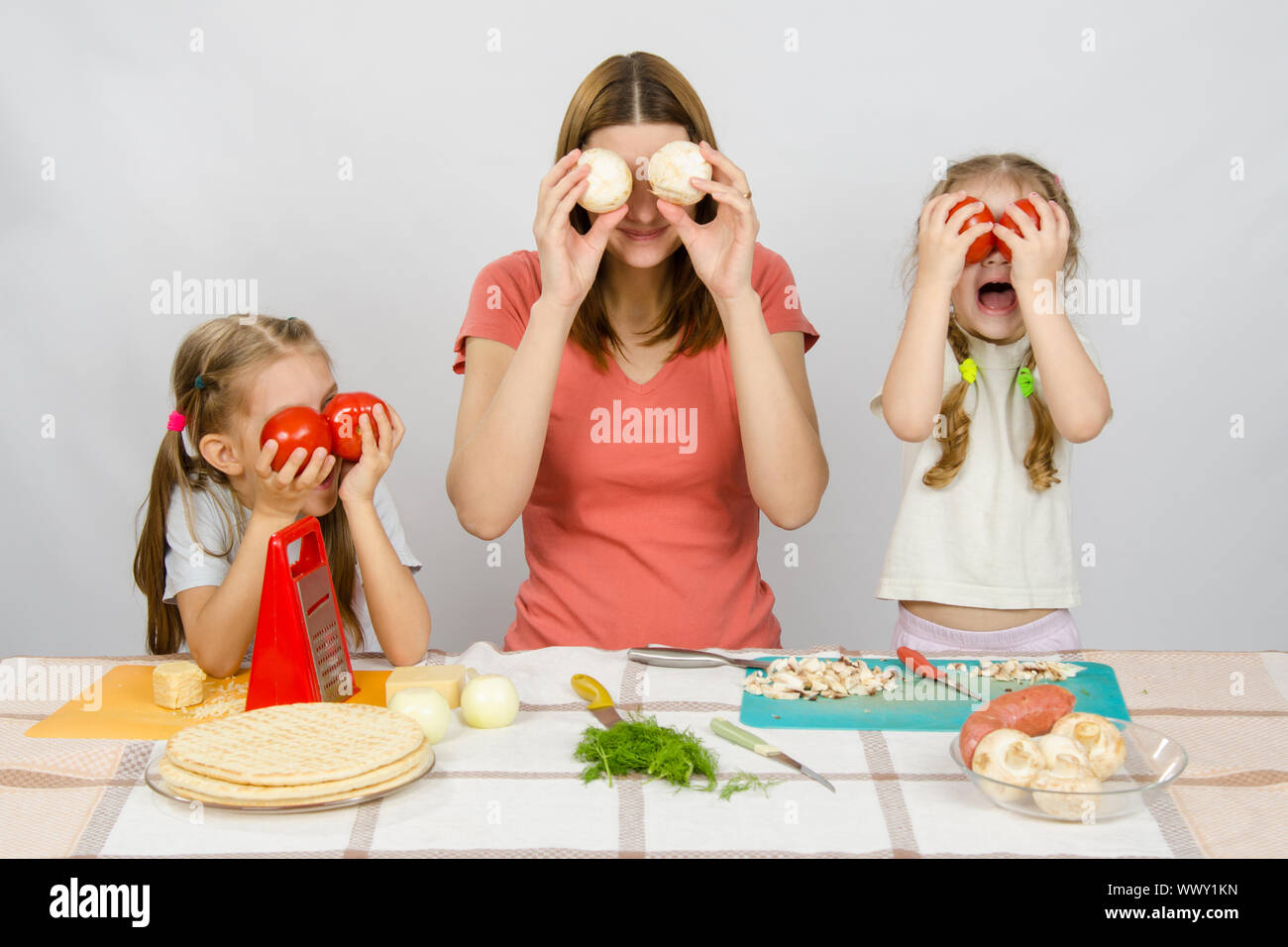 Mama mit zwei kleinen Mädchen, die Spaß am Küchentisch spielen mit Gemüse Stockfoto