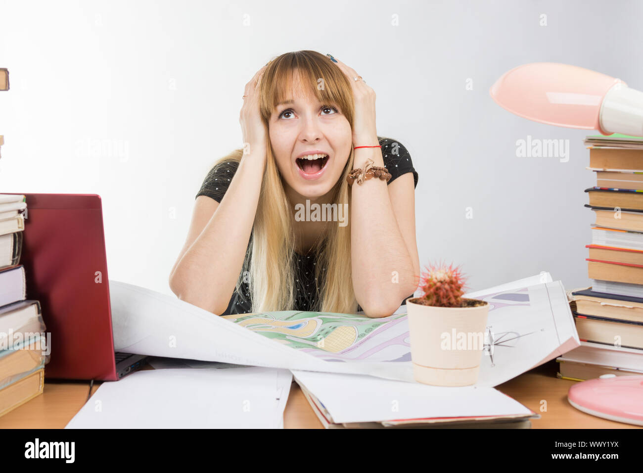 Mädchen-Design-Student an einem Schreibtisch mit einem Stapel Bücher und Projekte in ihrer Verzweiflung packte den Kopf Stockfoto