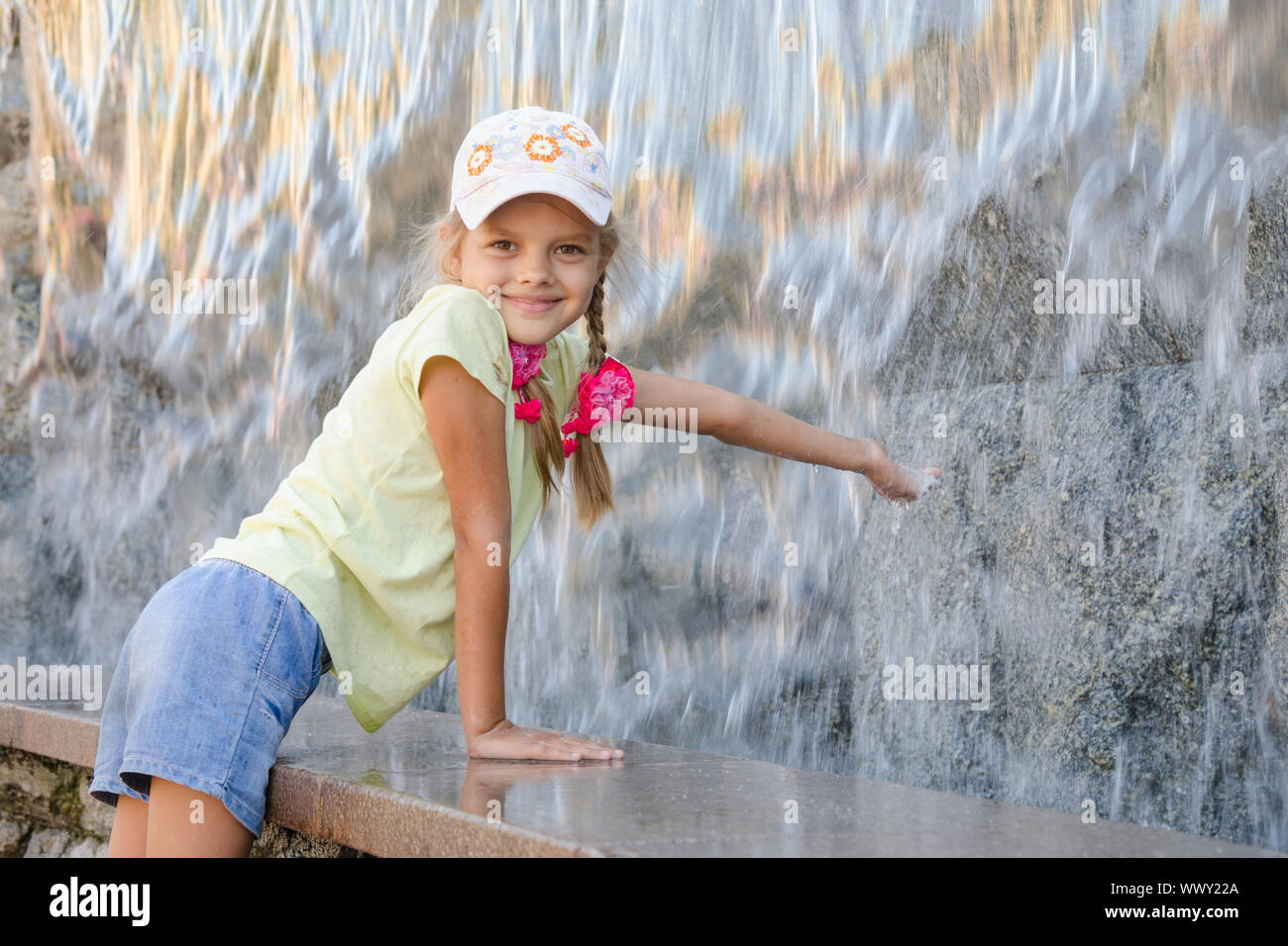 Mädchen im Sommer-Kleider mit einem Lächeln erstreckt sich seine Hand auf den künstlichen Wasserfall Wasser Stockfoto