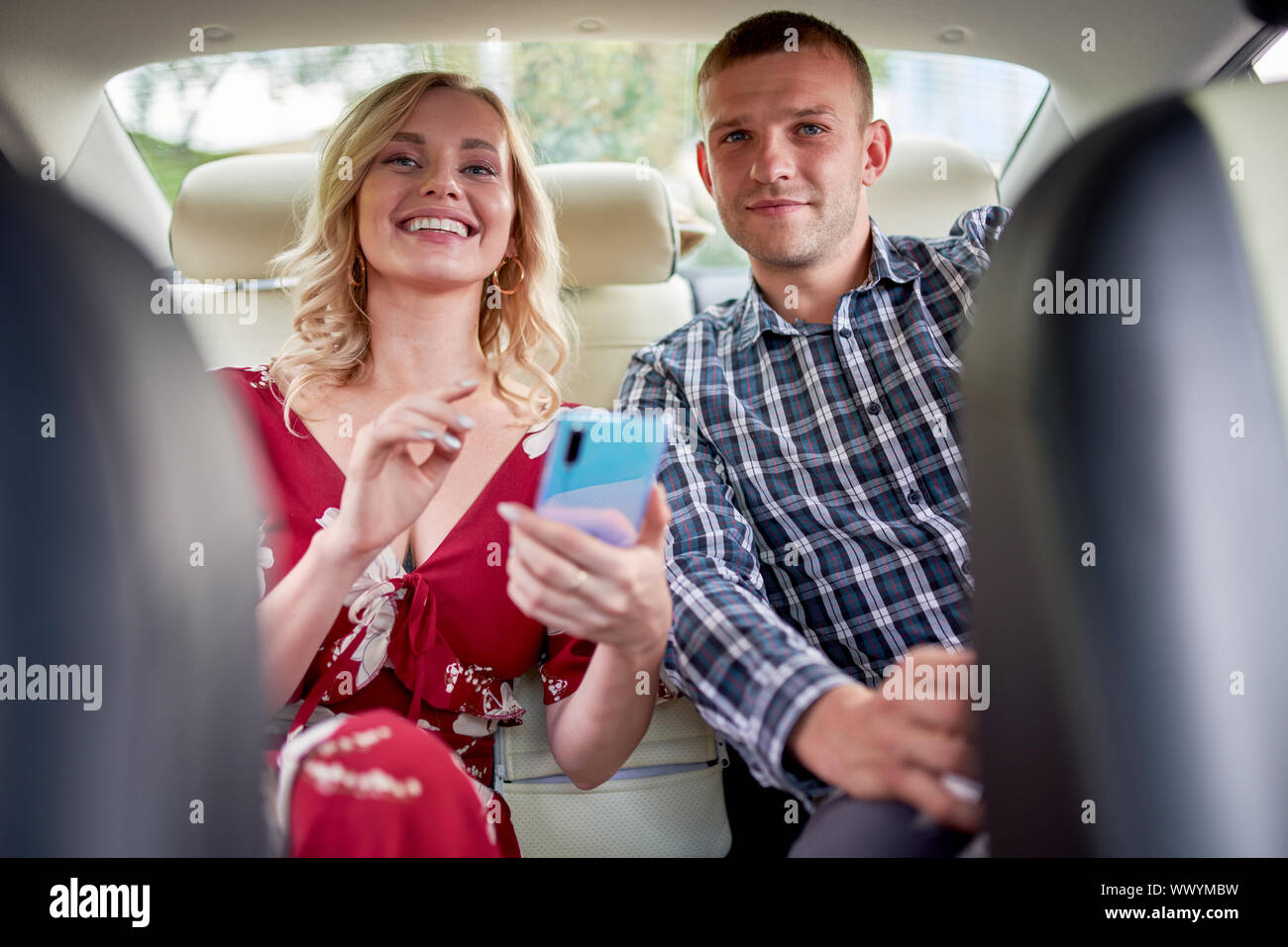 Bild der lächelnde Frau und Mann mit Handy in der Hand in den Rücksitz des Autos während der Sitzung Stockfoto