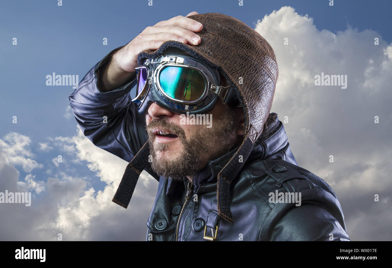 Alte Flugzeug Pilot auf dem Hintergrund der Gewitterwolken mit Ausdrucksstarken Gesicht. Gläser und alter Hut mit schwarzem Leder Jacke Stockfoto