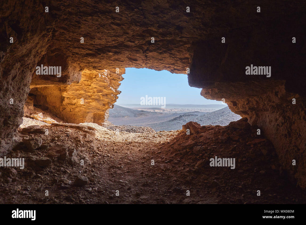 Blick aus dem Inneren der Höhle auf die steinige Wüste in der Sahara im Sudan liegen unter einem glitzernden Sonne. Stockfoto