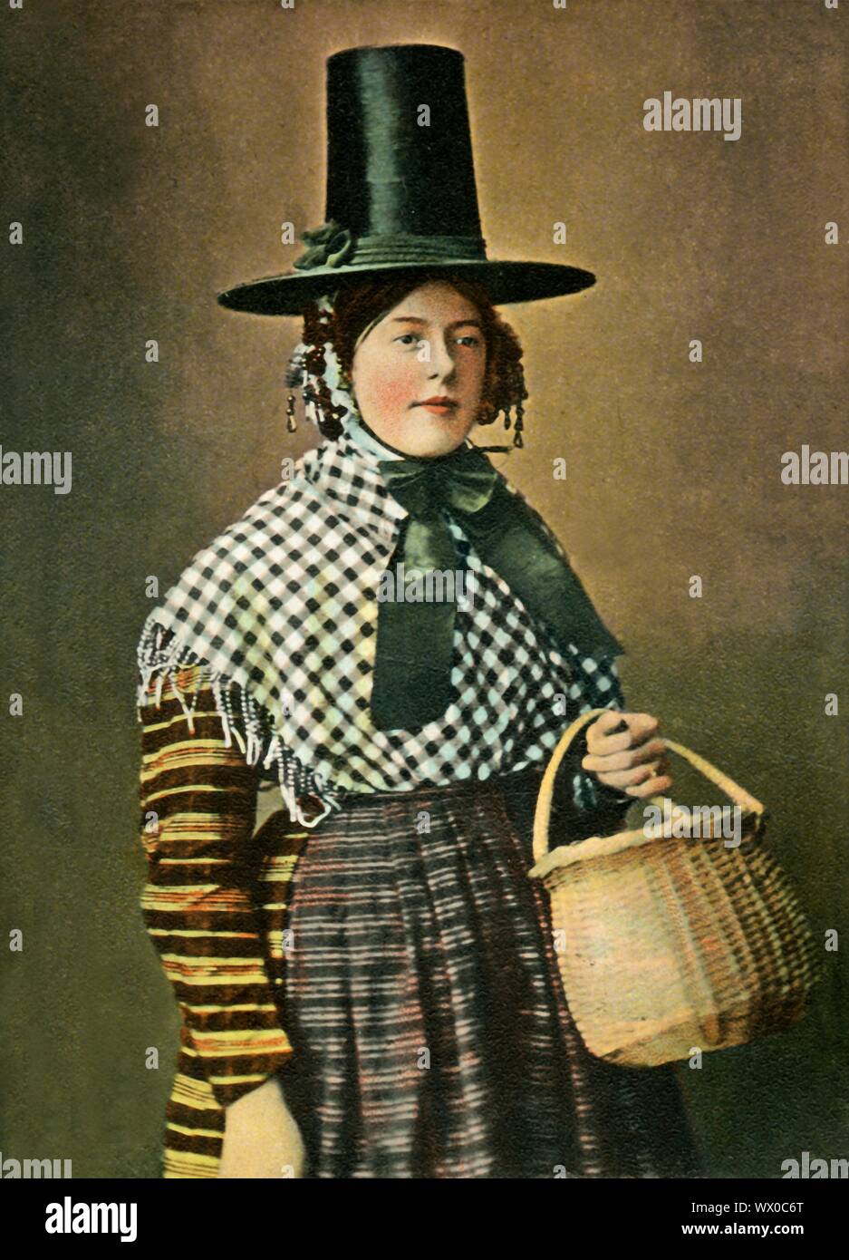 "Ein Waliser Kostüm', c 1904. Frau in Welsh National dress, mit hohen Hut, Schal, gestreifte Bluse und Schürze, die einen Korb. Hand - farbige Postkarte. [Bildliche Stationery Co Ltd., London, c 1904] Stockfoto