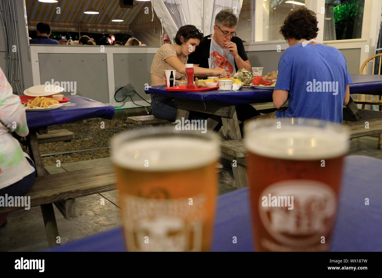 Eine Familie von drei genießen Meeresfrüchte in Arnold's Hummer & Clam Bar mit zwei Gläser Bier im Vordergrund. Eastham. Cape Cod. Massachusetts. USA Stockfoto
