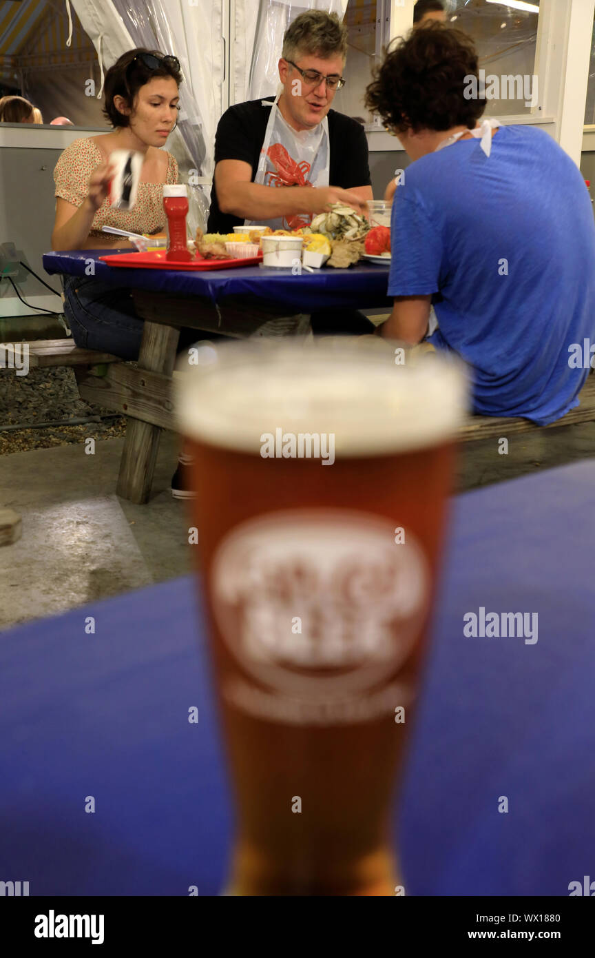 Eine Familie von drei genießen Meeresfrüchte in Arnold's Hummer & Clam Bar mit einem Glas Bier im Vordergrund. Eastham. Cape Cod. Massachusetts. USA Stockfoto