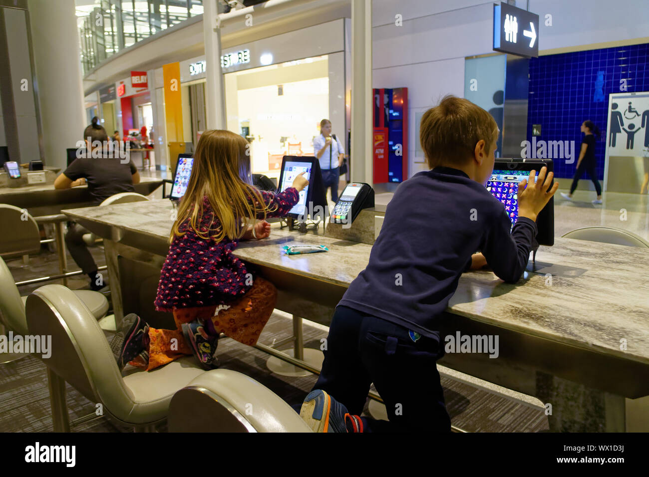 Sie Kinder spielen mit den öffentlichen Gebrauch ipads im Abflugbereich von Toronto Pearson Flughafen Stockfoto