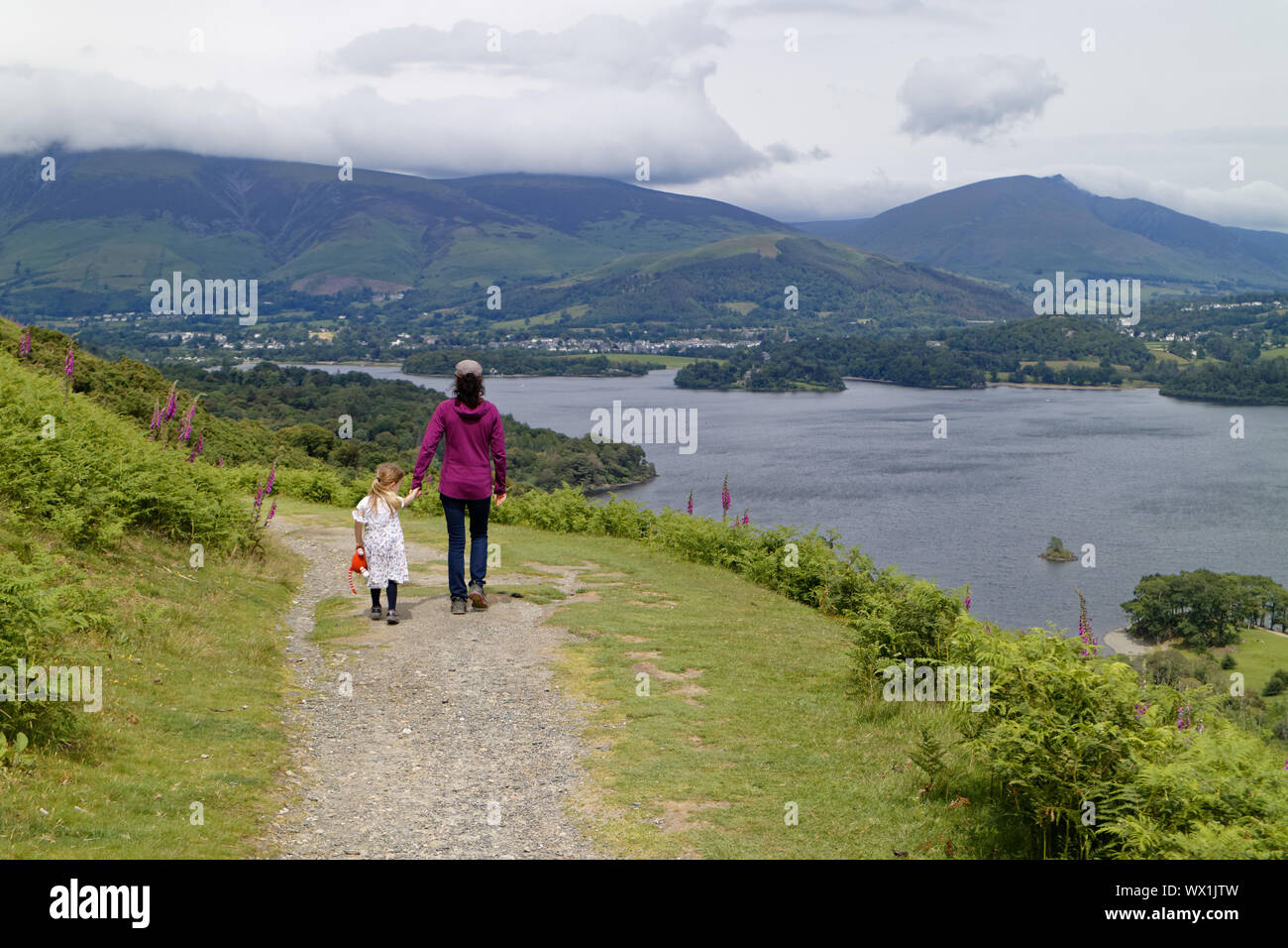 Mutter und Tochter gehen Hand in Hand im Lake District mit Derwent Water jenseits, Cumbria, Großbritannien Stockfoto