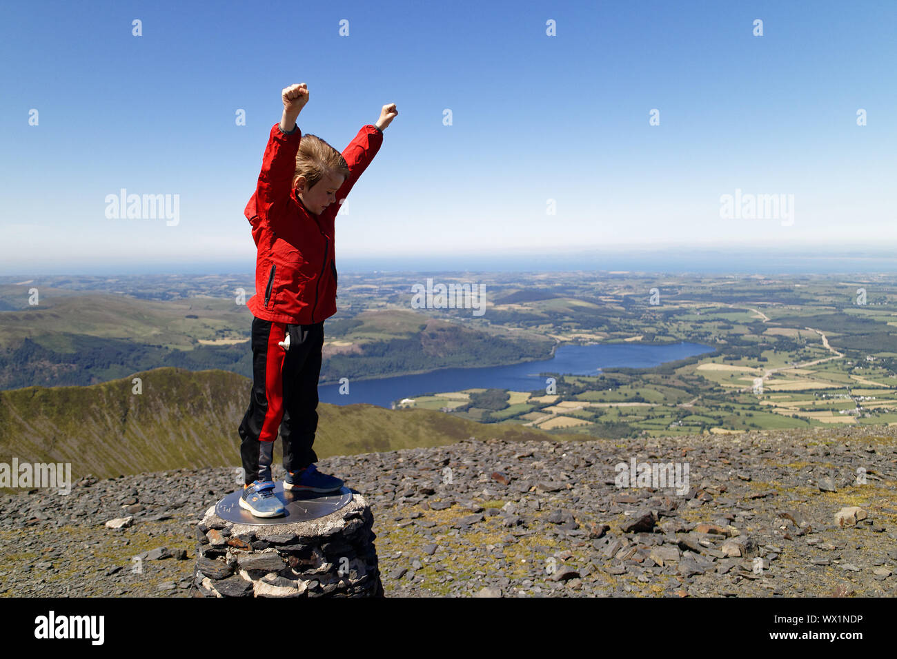 Ein Junge (7 Jahre alt) feiert auf dem Gipfel des Skiddaw, ein Berg im Lake District, Cumbria, Großbritannien Stockfoto