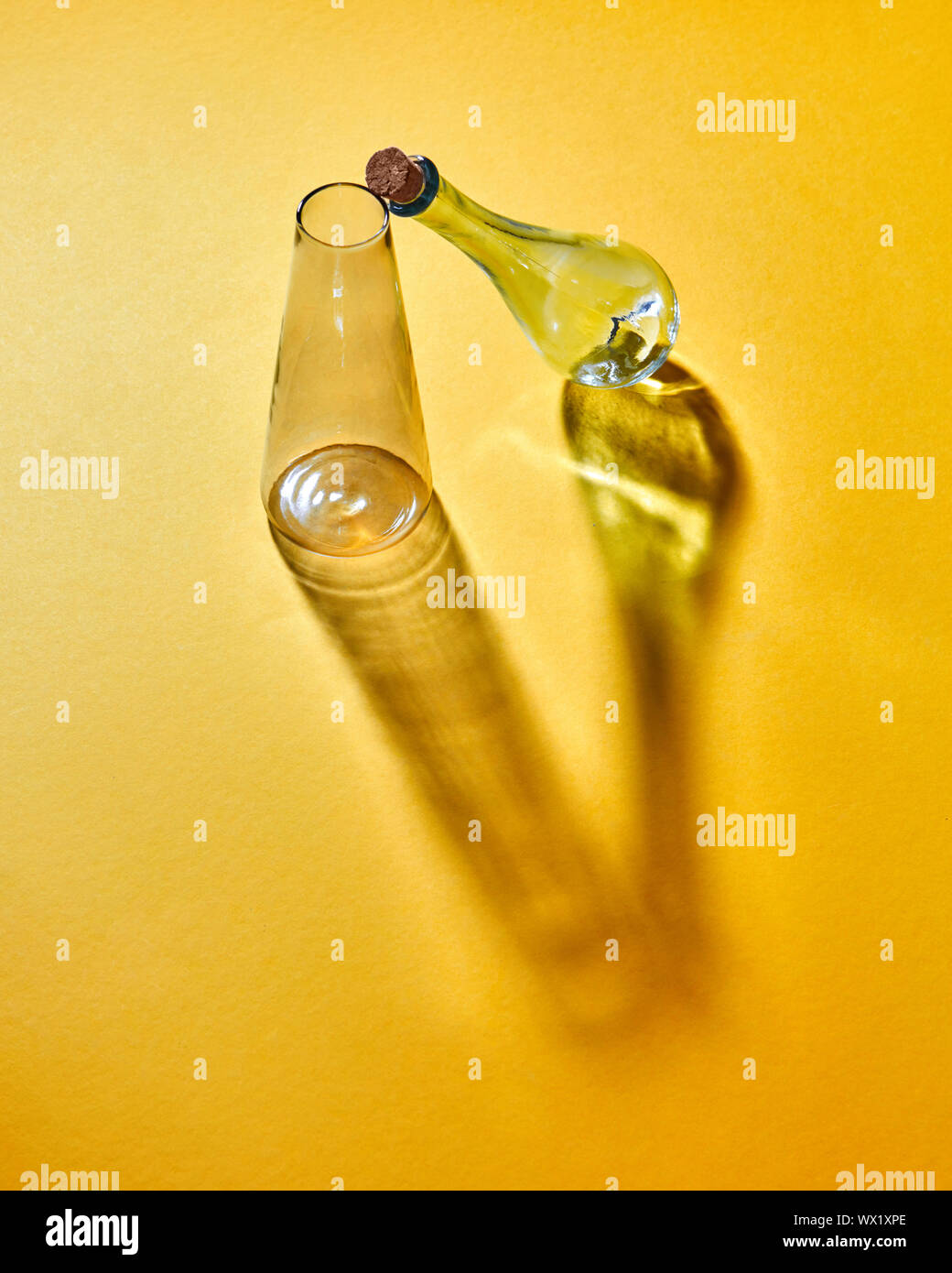 Zwei Glasflaschen mit sich kreuzenden lange Schatten und Reflexionen auf gelbem Papier. Stockfoto