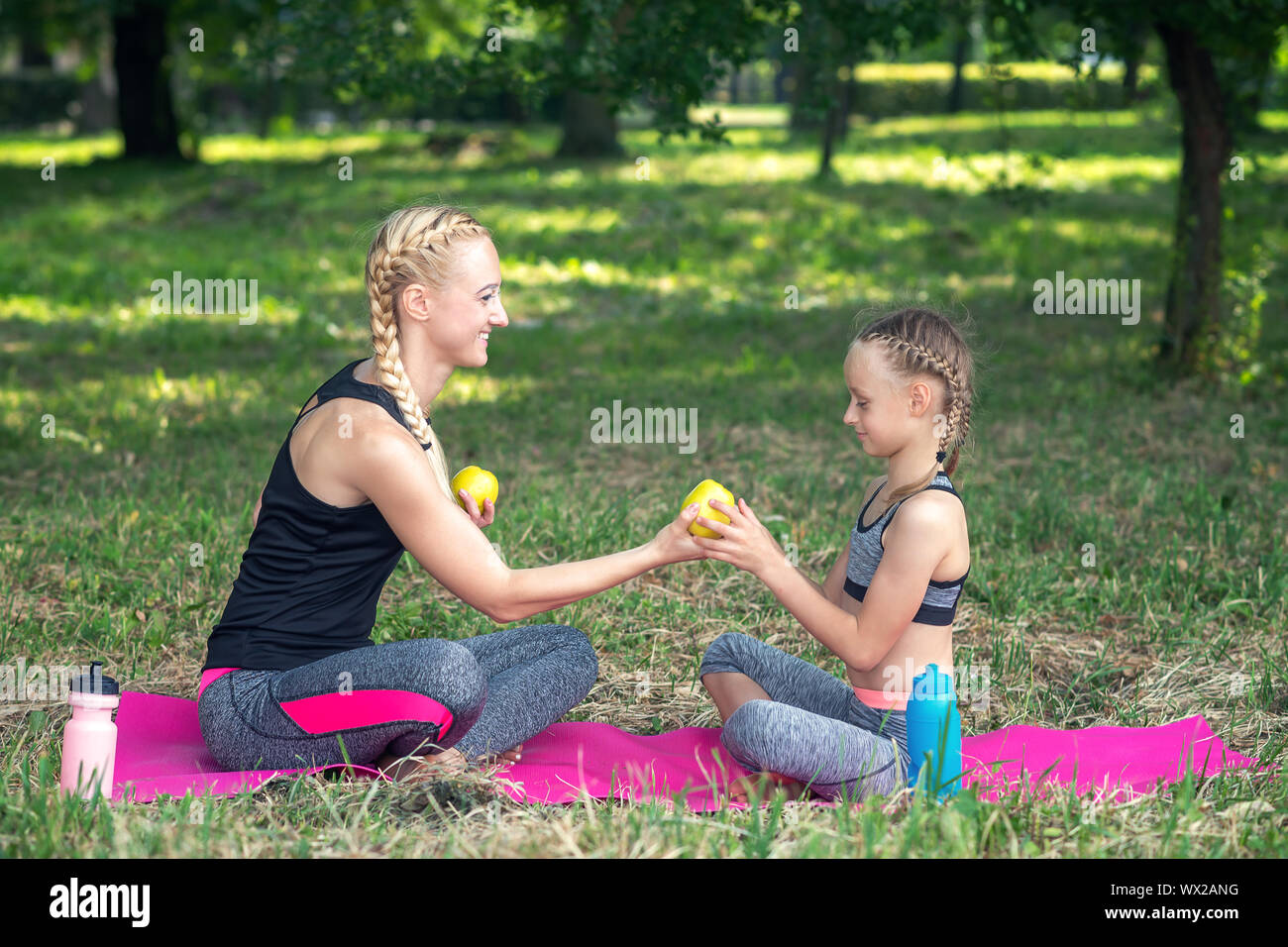 Sportliche Mutter schenkt Frische grüne Apple ihre kleine Tochter auf der Rolle Matte im Park, gesunde Ernährung Konzept Stockfoto