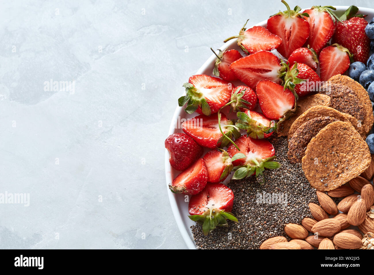 Weiße Platte mit natürlichen Zutaten zum Kochen Diät vegan Essen - oatflakes, Erdbeere, Chia Samen, Nüsse, Mandeln crunchies Stockfoto