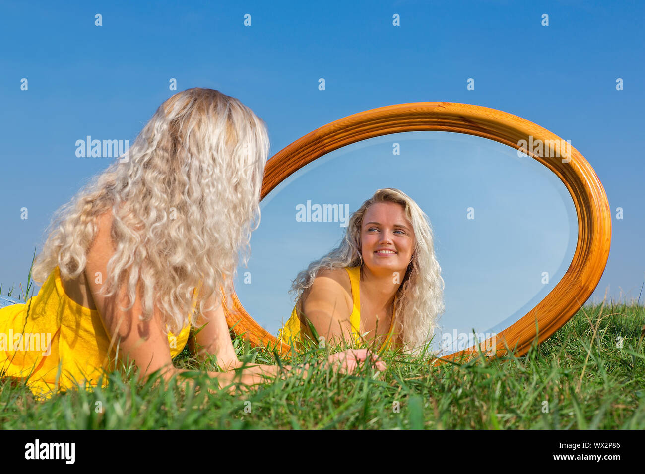 Junge blonde Frau im Gras liegend mit Spiegel Stockfoto