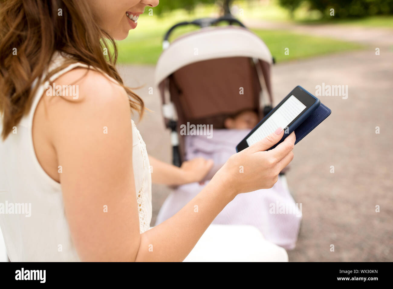 Mutter mit Kinderwagen lesen Internet buchen im Park Stockfoto
