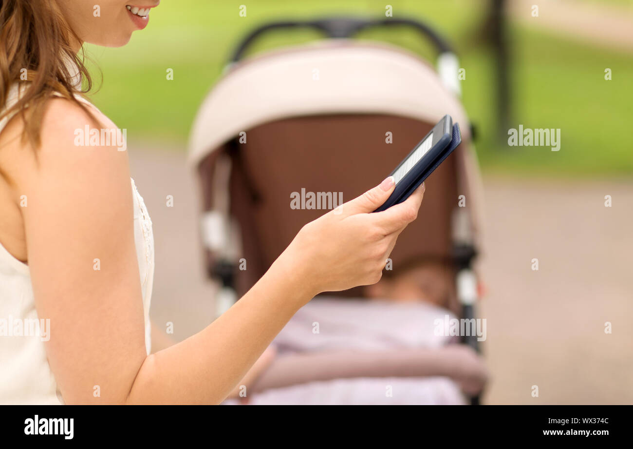 Mutter mit Kinderwagen lesen Internet buchen im Park Stockfoto