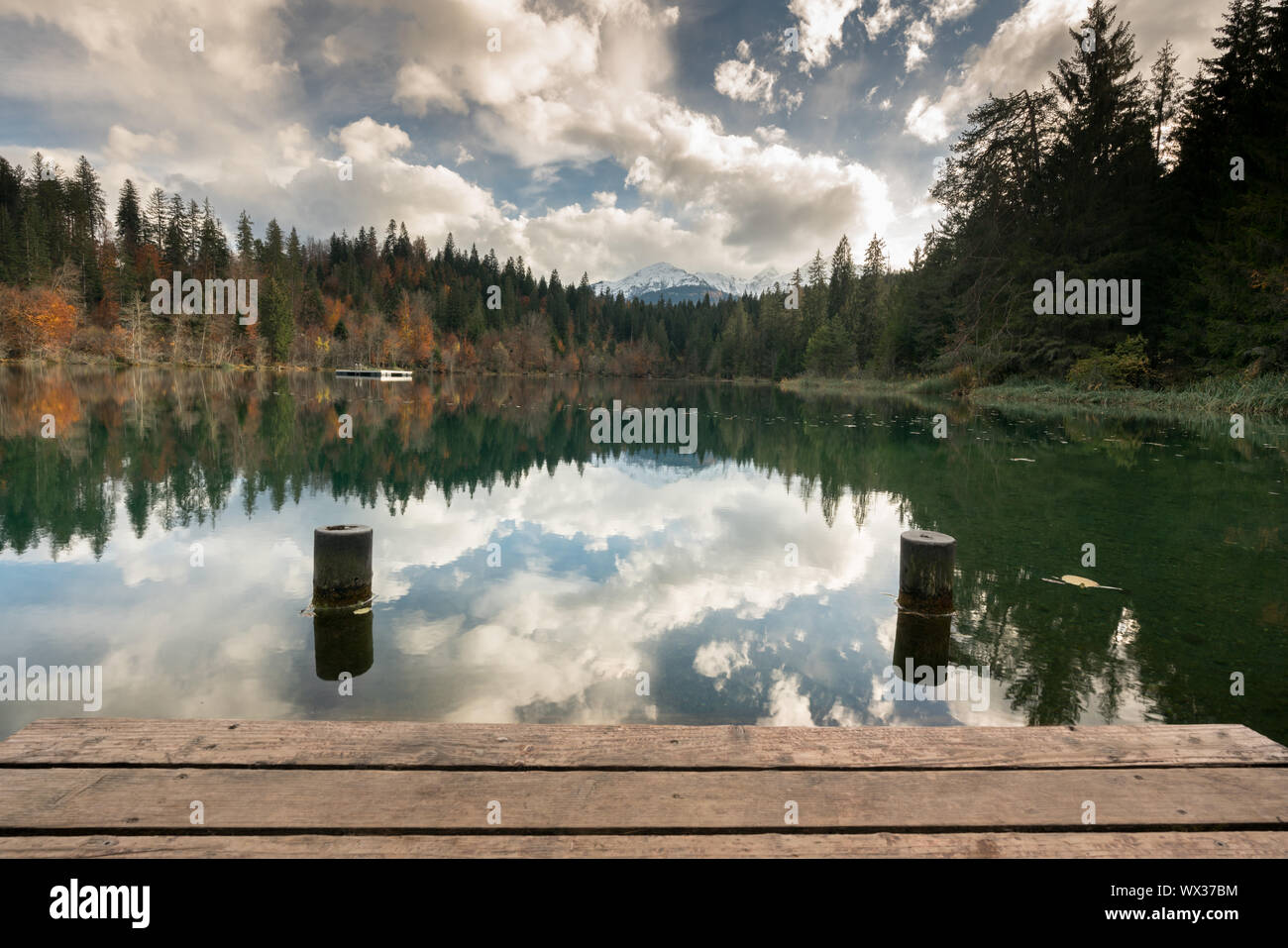 Hölzerne Seebrücke und Promenade mit Dock Pylonen am Rande eines idyllischen Bergsee umgeben von Fal Stockfoto