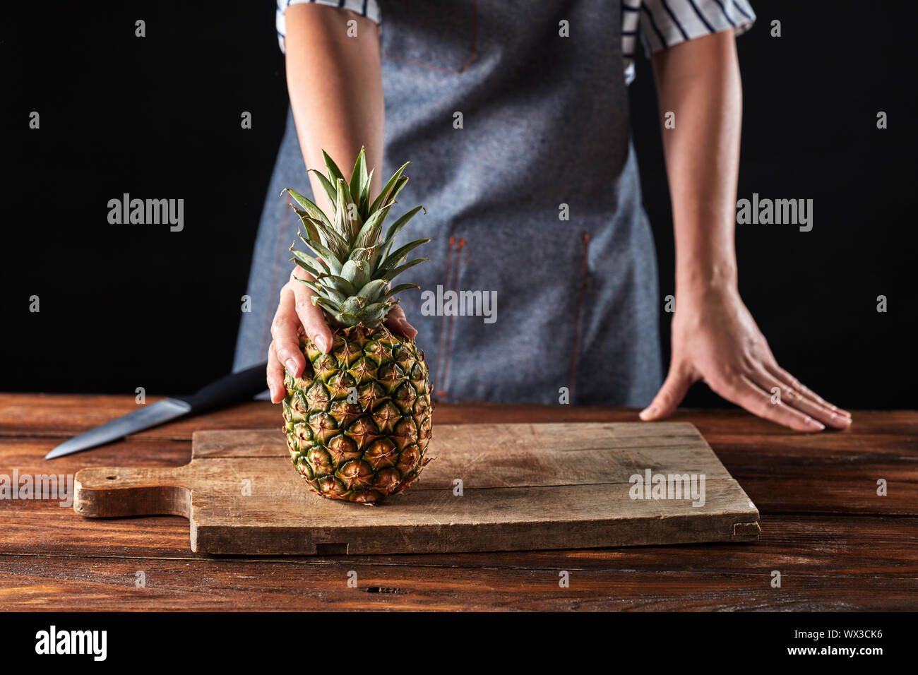 Die Hand einer Frau, die eine reife Ananas auf einem alten Holzplatte auf dem Küchentisch um einen dunklen Hintergrund zu kopieren. Stockfoto