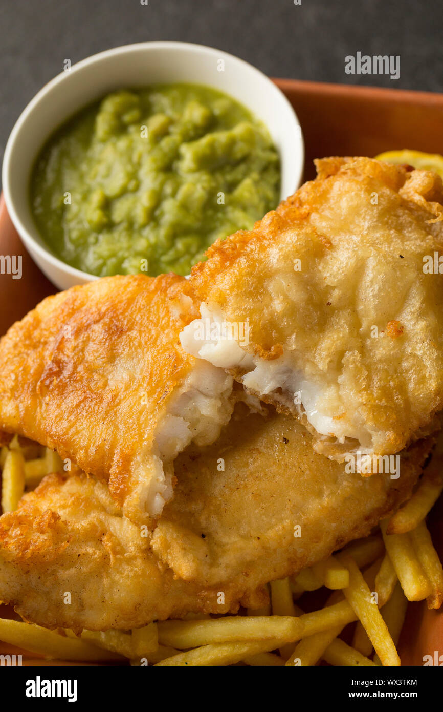 Ein hausgemachtes Filet von der Linie gefangen Pollack Pollachius pollachius, die in Teig getaucht vor dem Frittieren und Servieren mit Backofen Chips und Stockfoto