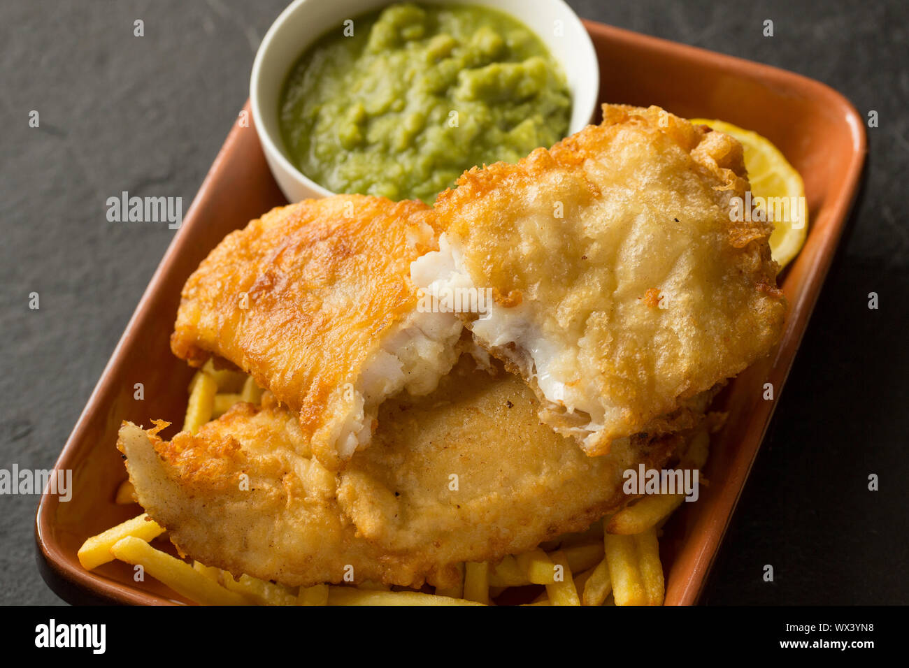 Ein hausgemachtes Filet von der Linie gefangen Pollack Pollachius pollachius, die in Teig getaucht vor dem Frittieren und Servieren mit Backofen Chips und Stockfoto