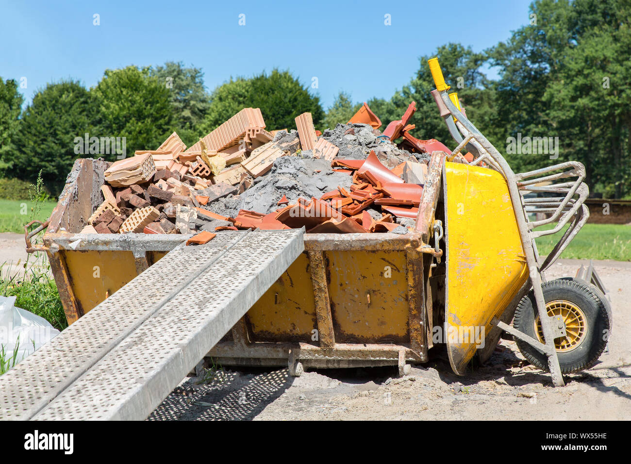 Behälter mit Schutt und Schubkarre außerhalb Stockfoto