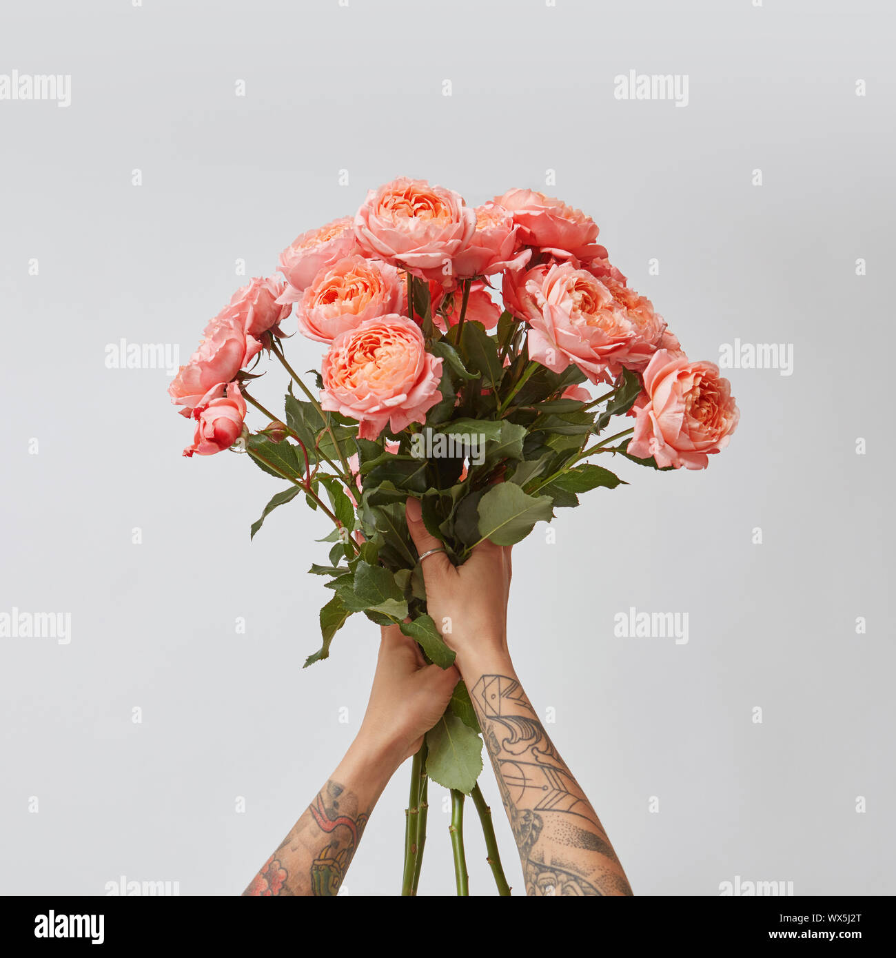 Girl's Hände mit Tattoo halten Sie einen Strauß mit frischen Rosen in einer Farbe des Jahres 2019 Lebende Korallen Pantone auf grauem Hintergrund. Stockfoto