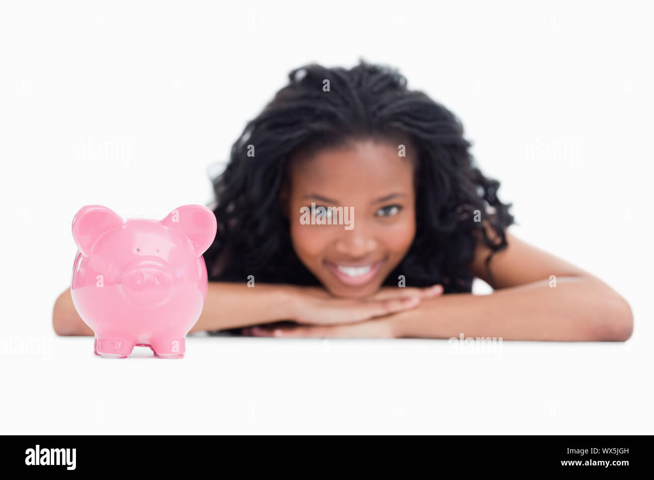 Eine junge lächelnde Mädchen den Kopf auf die Hände mit einem sparschwein vor ihr vor einem weißen Hintergrund Stockfoto