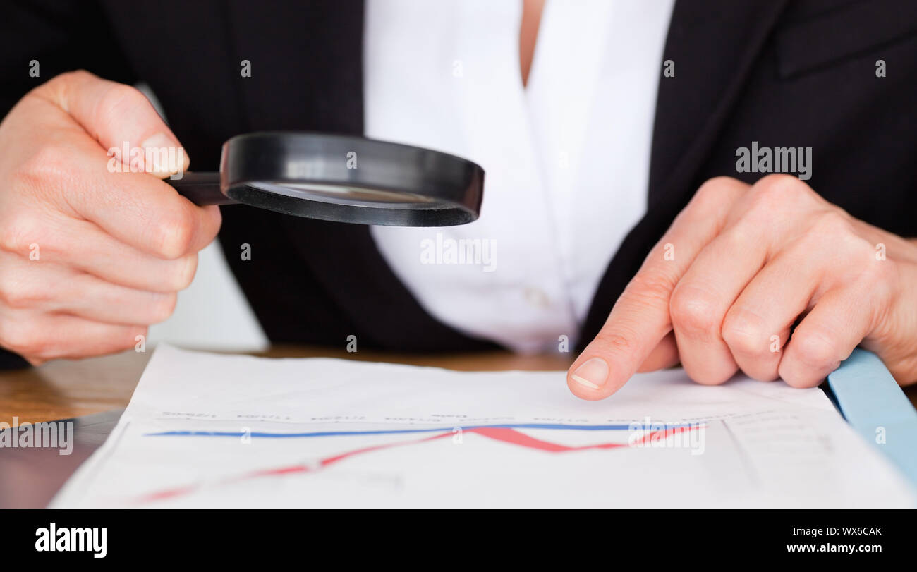 Weibliche Hände halten eine Lupe über ein Diagramm Stockfoto