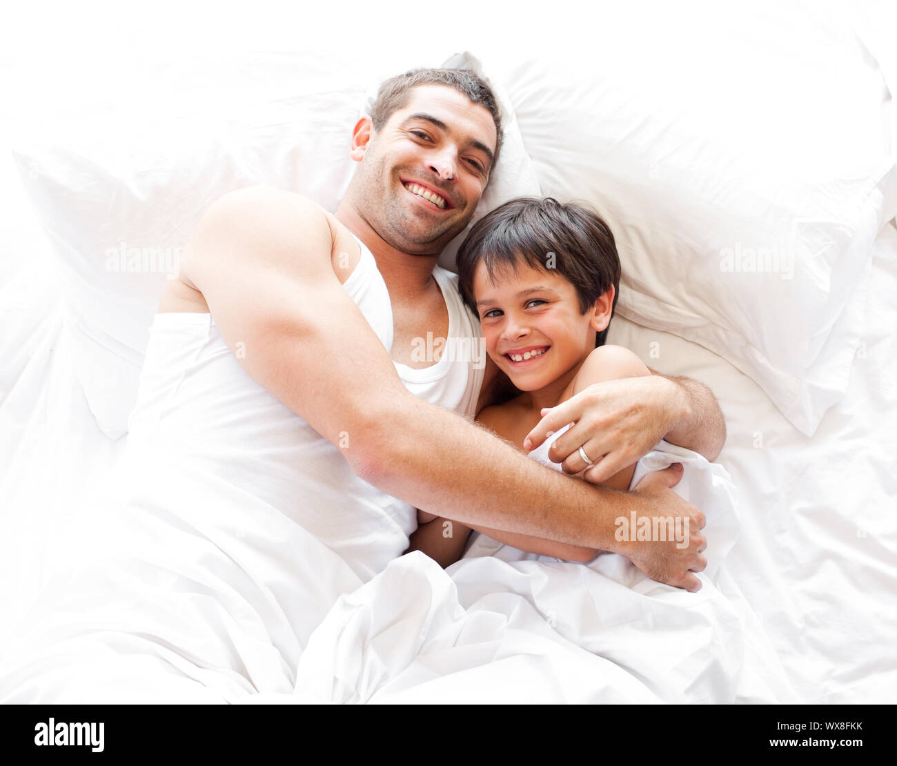 Glücklicher Vater und Sohn auf dem Bett in die Kamera schaut Stockfoto