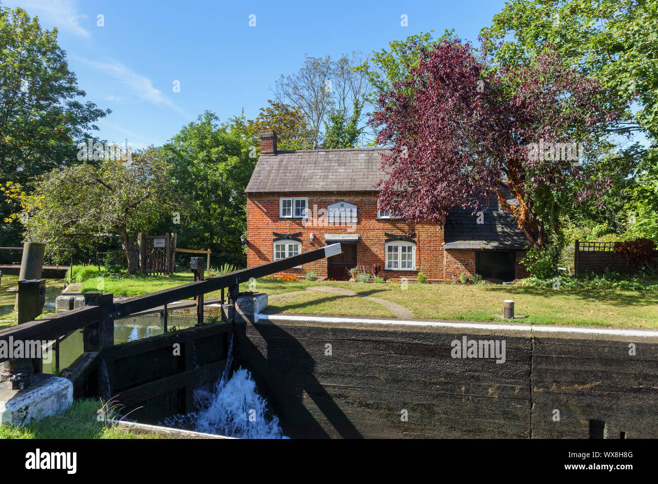 Blick auf New Haw Schloss und der historische Schleusenwärter Cottage auf dem Fluss Wey (Wey Navigationen) bei New Haw, Surrey, Südost England Stockfoto