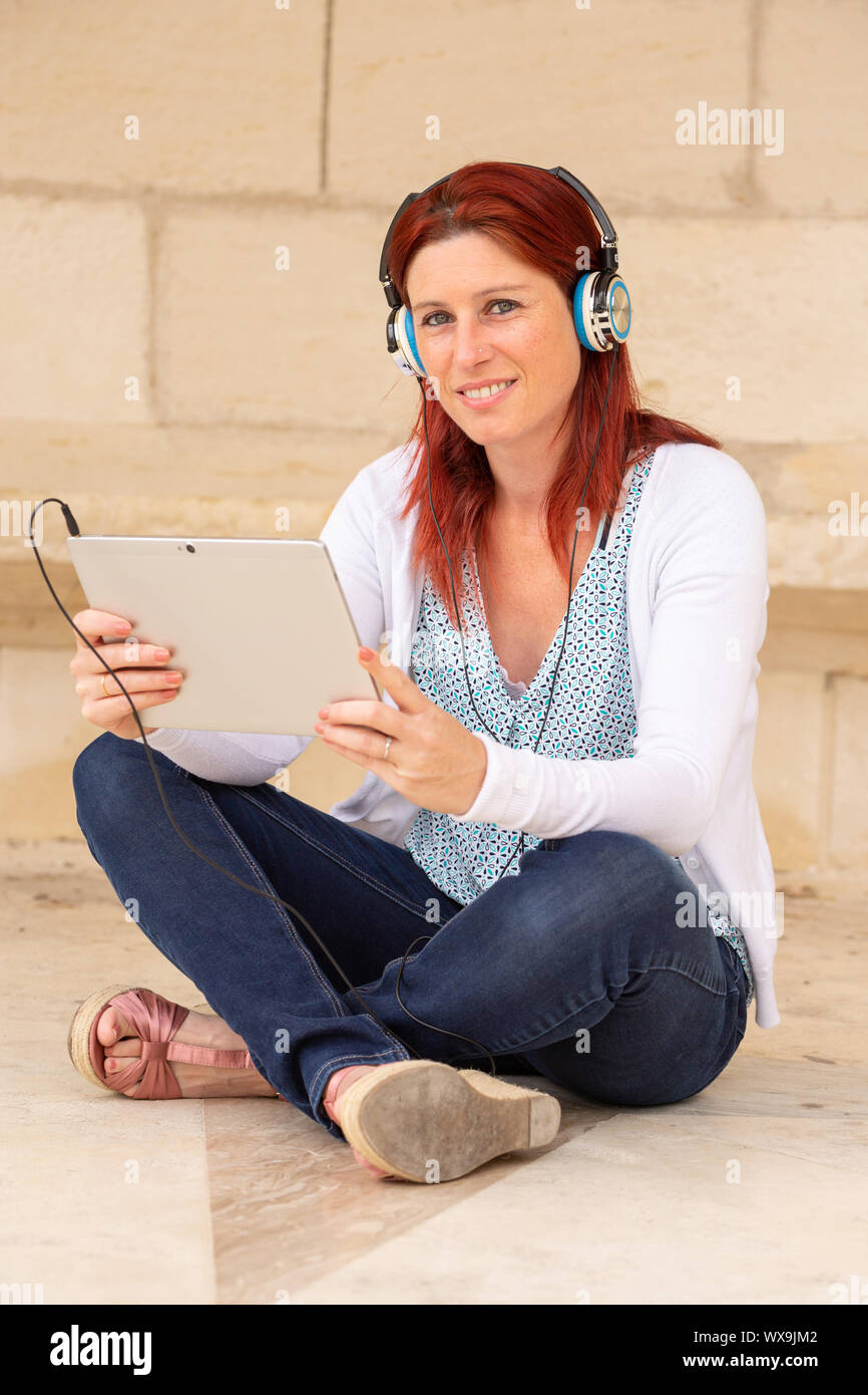 Hübsches Lächeln rothaarige Frau auf dem Boden sitzend hören von Musik oder beim Anschauen eines Films auf einem Touch Pad Stockfoto