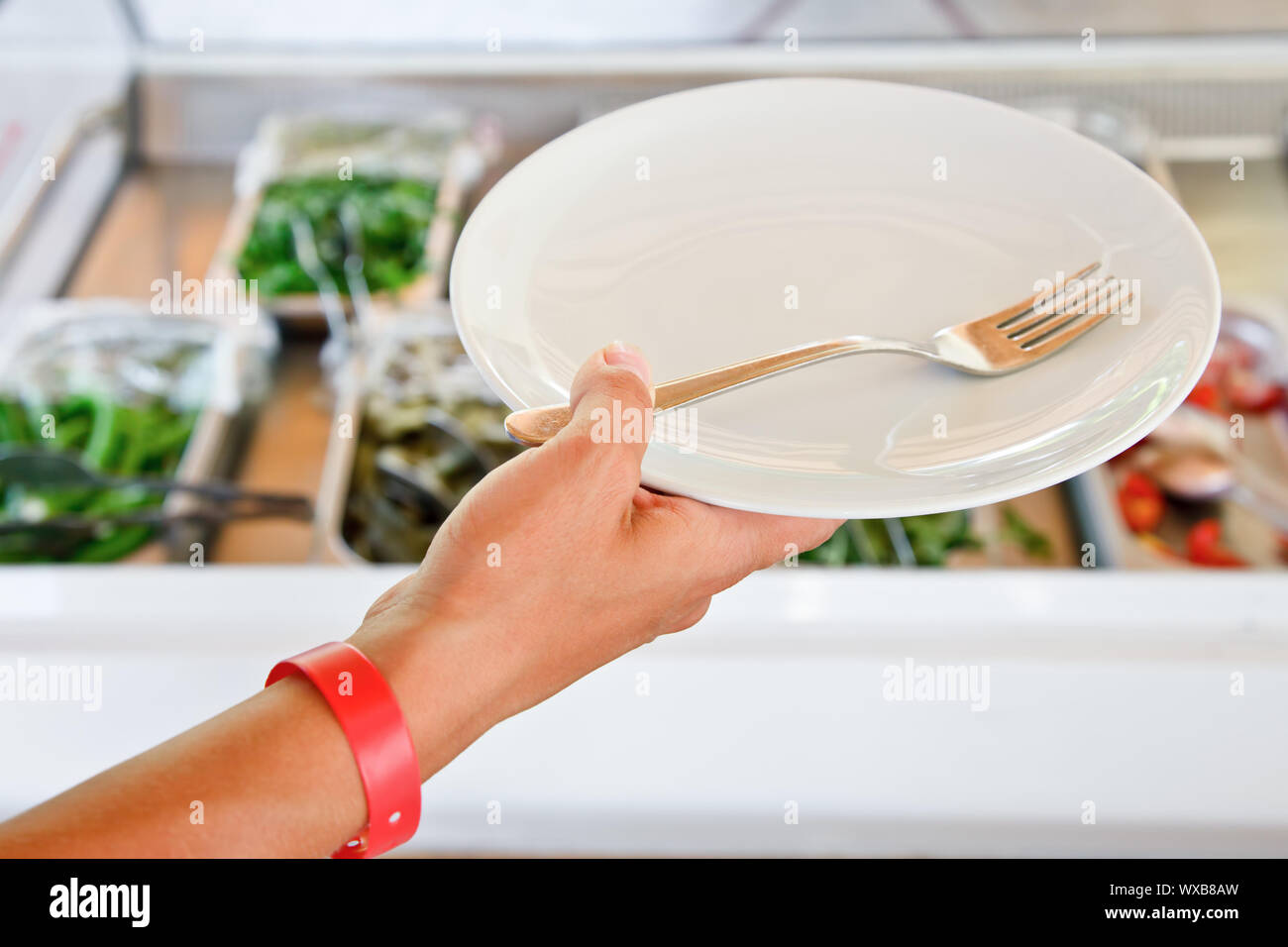 Hand tragen all-inclusive Armband Holding leeren Teller mit Gabel gegen vegetarisches Buffet Tisch Stockfoto