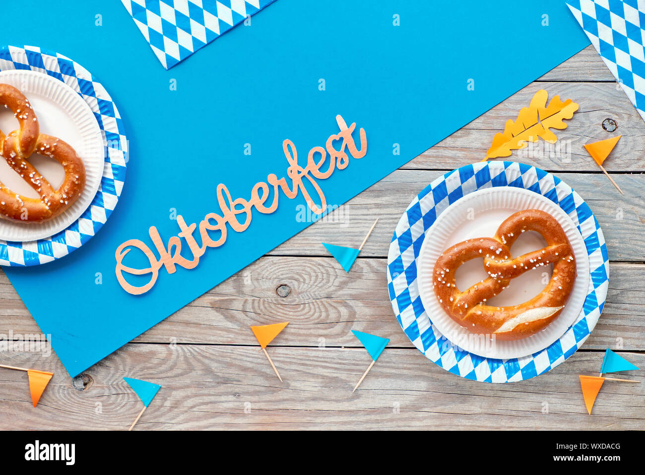 Oktoberfest, flach auf rustikalen Holztisch mit blauen Papier verteilt lagen, Brezeln auf das verfügbare Platten mit blau weiß Bayerische Muster, Dekorationsfahnen Stockfoto