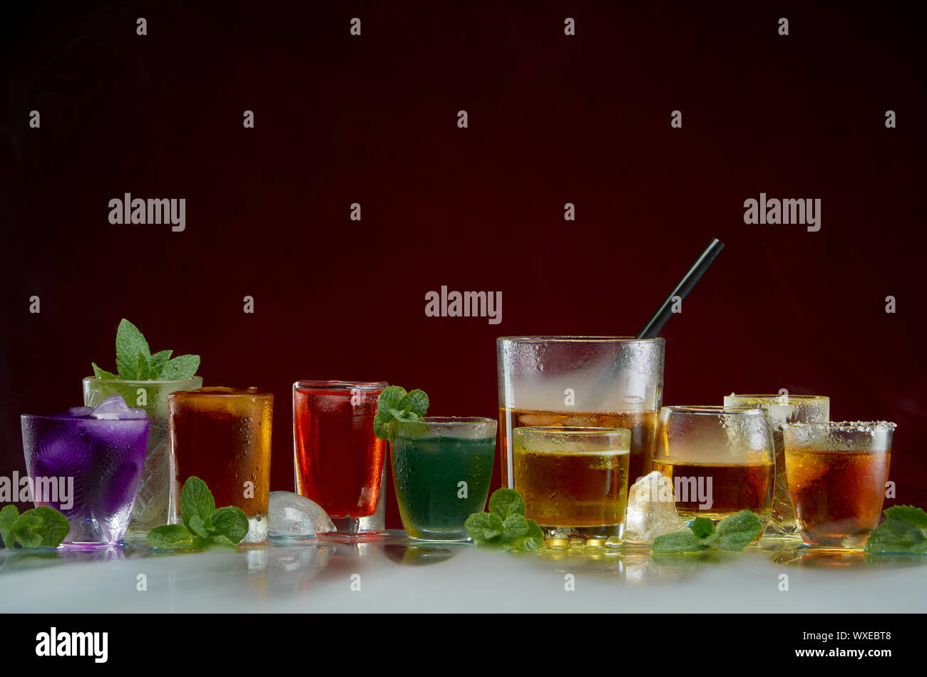 Gläser mit verschiedenen alkoholischen Getränken mit Eis und Minze auf rotem Hintergrund Stockfoto