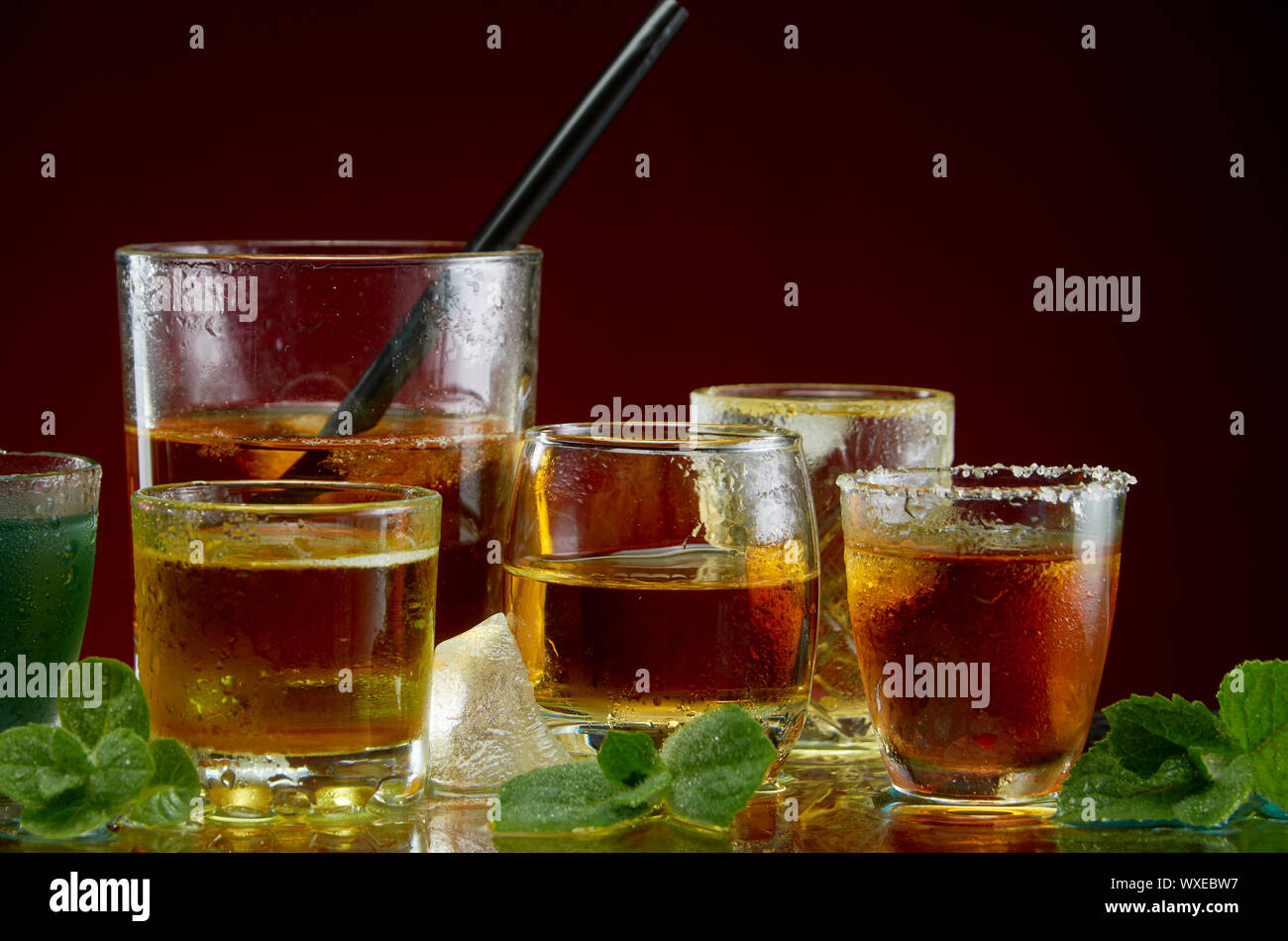 Verschiedene alkoholische Cocktails in klare Gläser mit Eis und Minze auf rotem Hintergrund Stockfoto