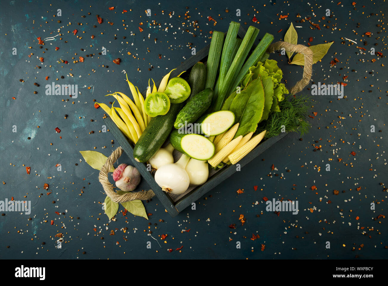 Das GEMÜSE IN DER BOX AUF DEM STEIN einen dunklen Hintergrund. Junge Kräuter Zwiebeln Knoblauch Grüne Bohnen gelber Mais ZUCCHINI HELLE SPIC Stockfoto