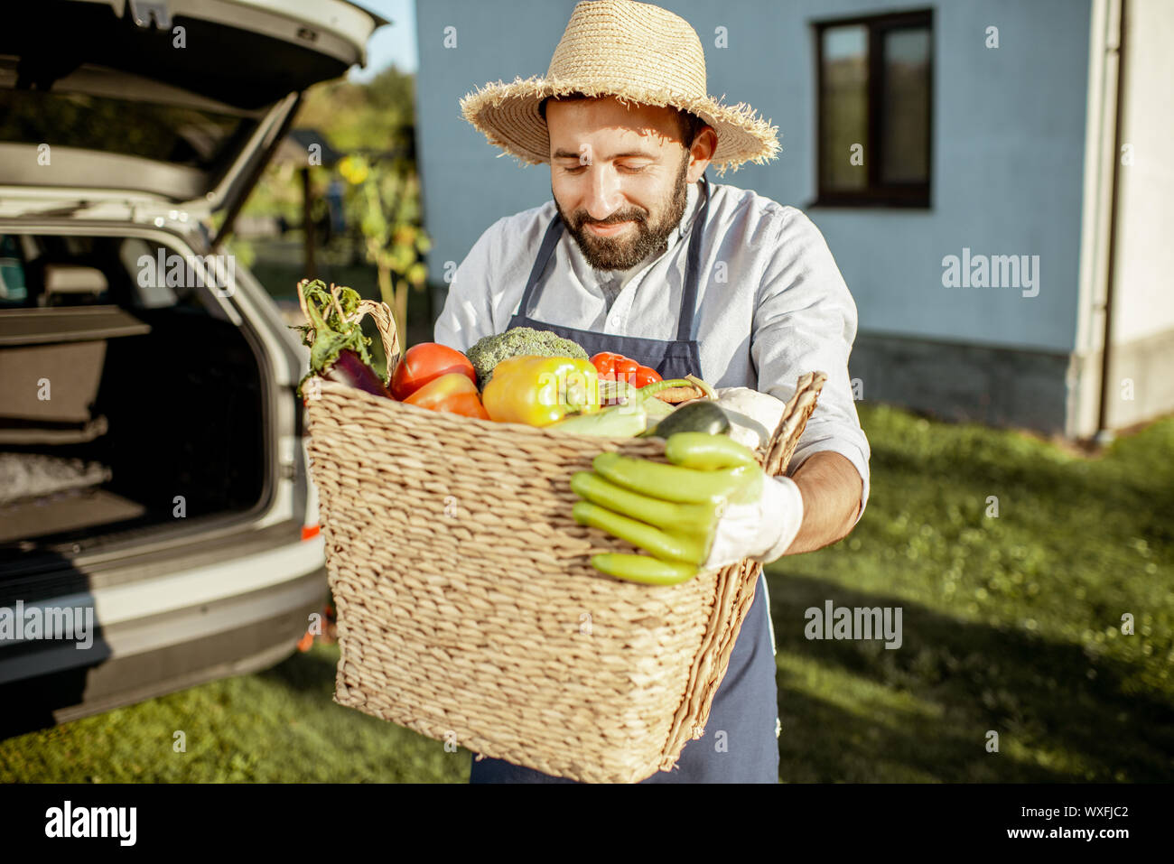 Porträt von einem gutaussehenden Mann mit Strohhut mit Korb voller frisch, Gemüse aus eigenem Anbau in der Nähe der Car auf dem Land Stockfoto
