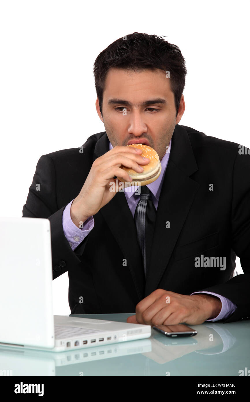 Geschäftsmann, einen Hamburger zu essen, an seinem Schreibtisch Stockfoto