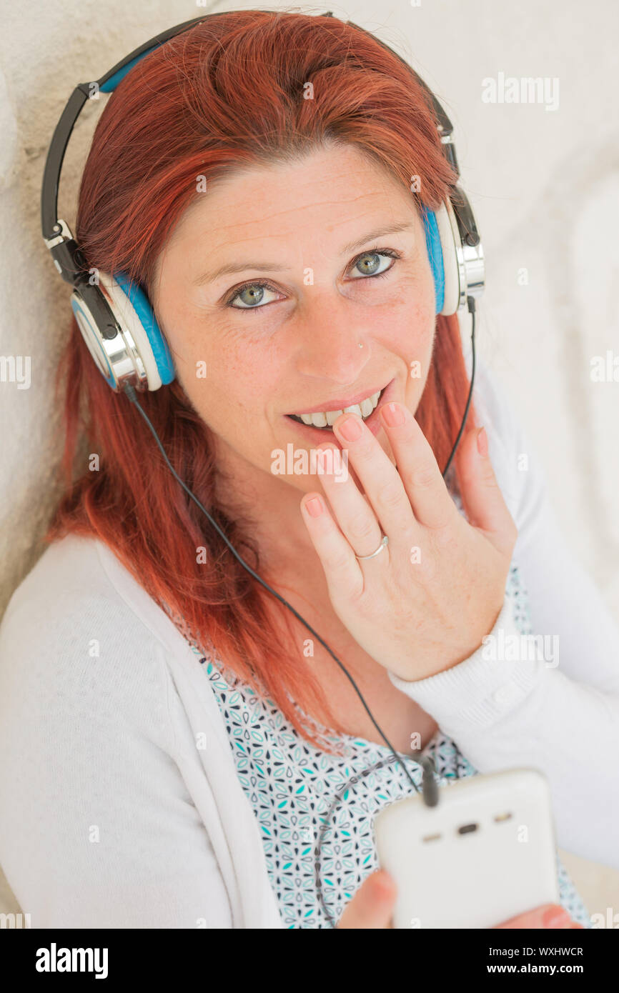 Hübsches Lächeln rothaarige Frau mit der Hand auf den Mund Wand hören die Musik auf Ihrem Telefon mit einem Headset Stockfoto