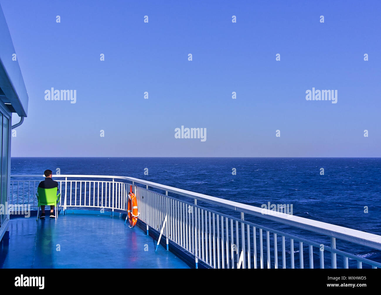 Mann sitzt auf Stuhl aus Kunststoff, die auf einem Schiff deck während der Fahrt im offenen Meer. Stockfoto