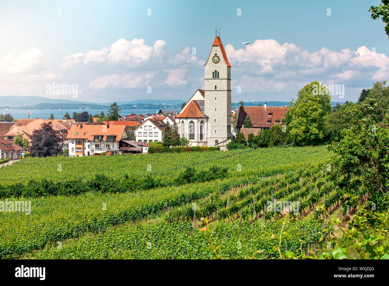 Panoramablick auf den Bodensee. Zeppelin, Apfelbäume und die Katholische Kirche St. Johann Baptist in Hagnau am Bild. Stockfoto