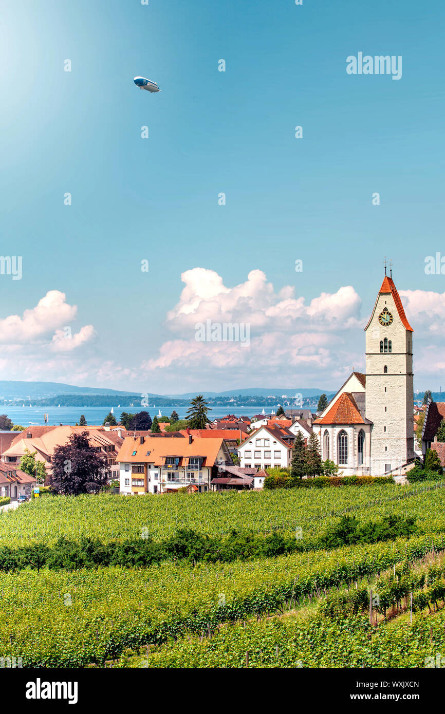Panoramablick auf den Bodensee. Zeppelin, Apfelbäume und die Katholische Kirche St. Johann Baptist in Hagnau am Bild. Stockfoto