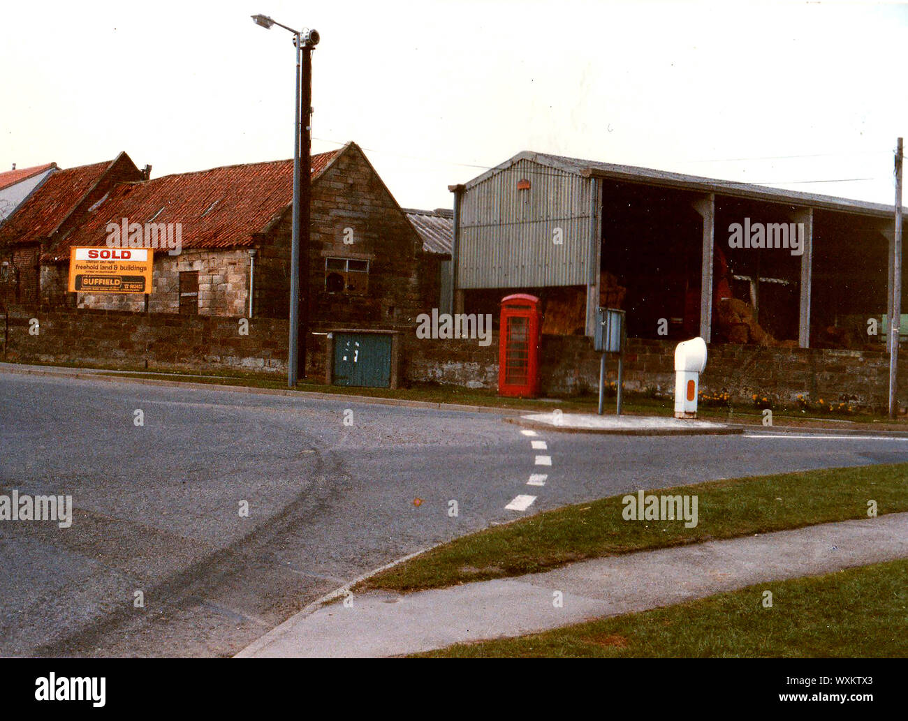 Juni 1986. Ehemaligen landwirtschaftlichen Gebäuden auf vier Fahrstreifen endet Kreisverkehr (Straße auf Serpentinen auf der rechten Seite), Whitby, Yorkshire, England, vor der Sanierung. Die Gegend am Rande der Stadt enthält jetzt Wohnimmobilien. Auf der Lamp Post können eine alte AIR RAID SIREN, gesehen werden und darunter eine traditionelle britische rote Telefonzelle. Stockfoto