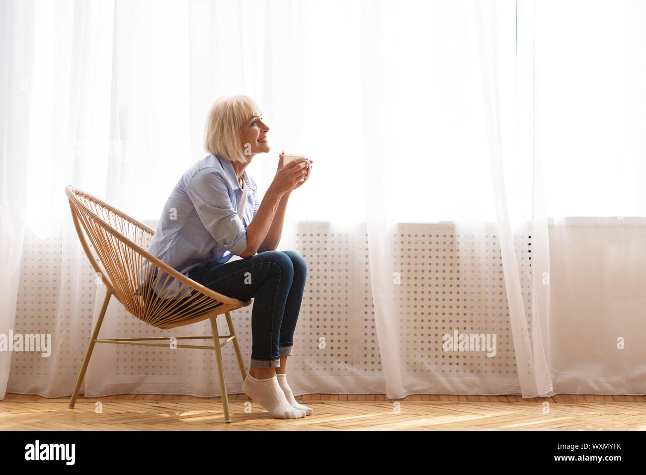 Ältere Frau sitzt auf der Stuhl vor das Fenster und Tee trinken. Stockfoto